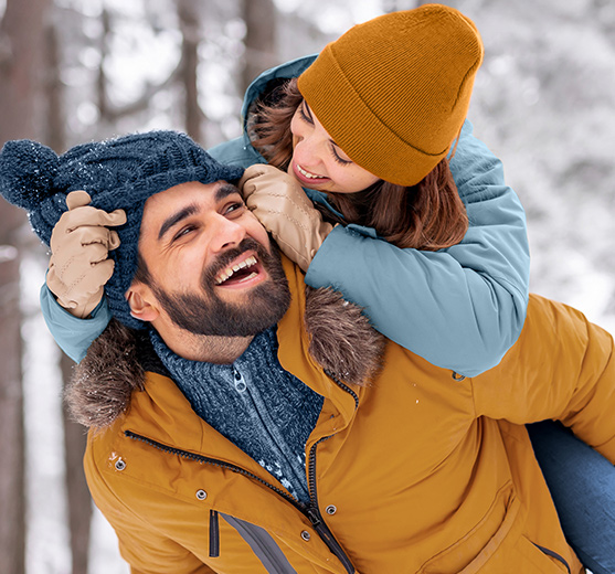 A couple bundled up in winter gear, smiling in the snow!