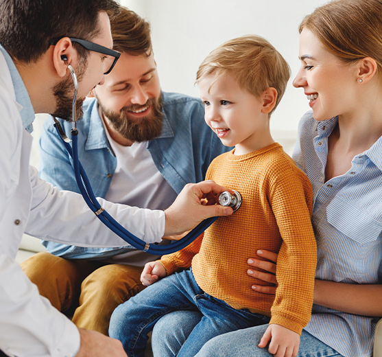 A young boy is at the doctor's with his parents. The doctor is using a stethoscope to hear the boy's heartbeat.